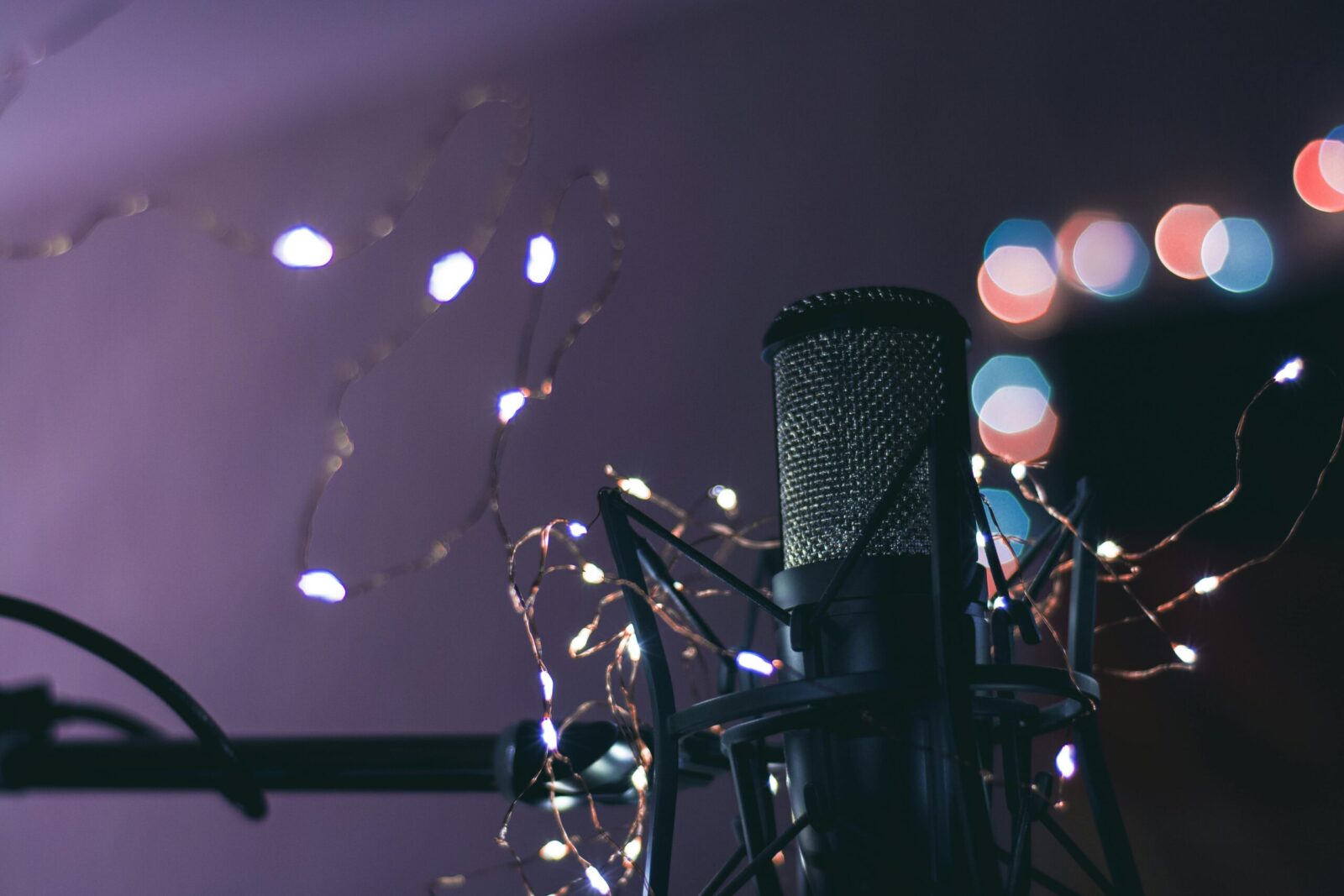 Condenser microphone surrounded by string lights creating a bokeh effect, ideal for studio and music themes.